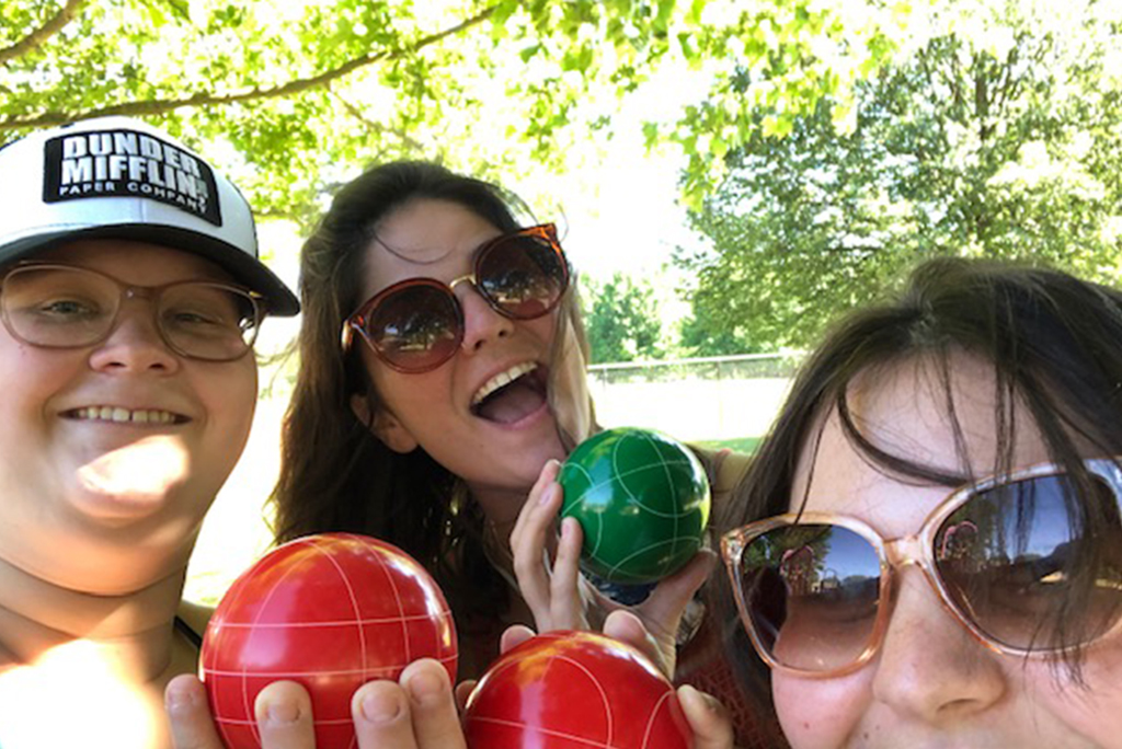 Three ladies hold up red and green bocce balls.