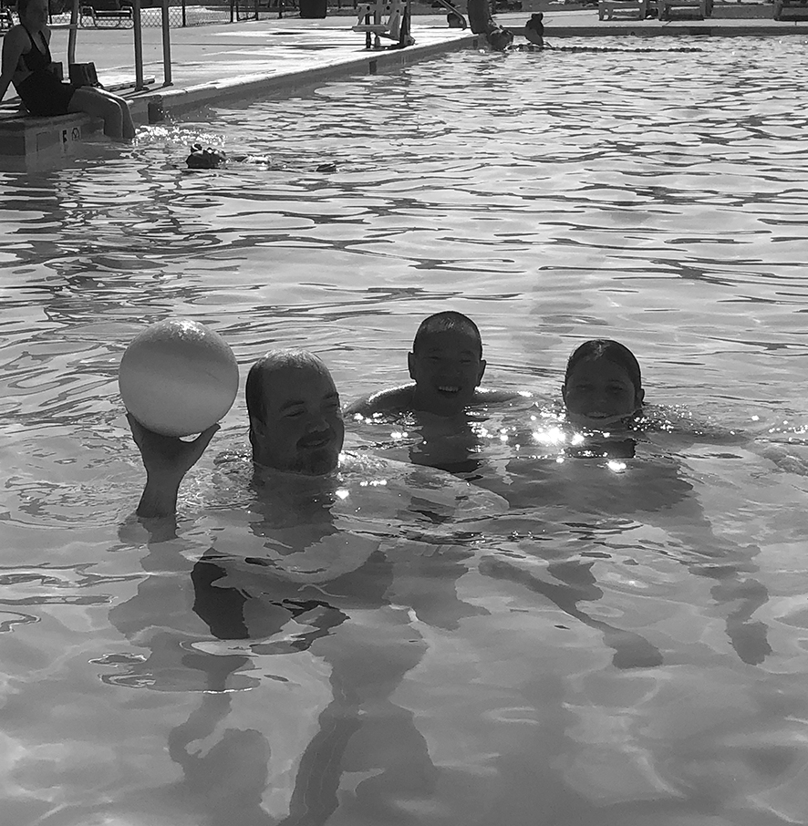 Three people swimming in a pool with a white ball.